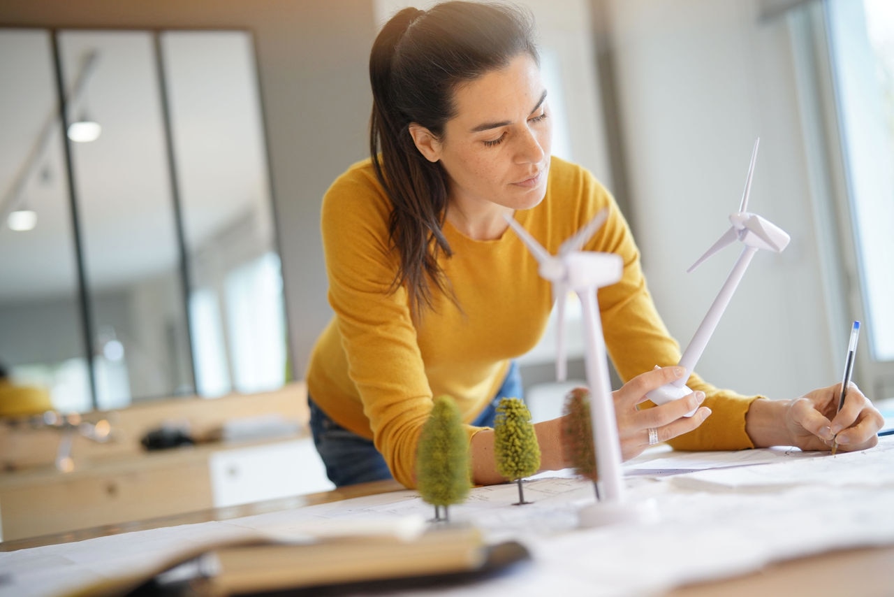 Stunning wind turbine engineer with cellphone planning wind farm placement.